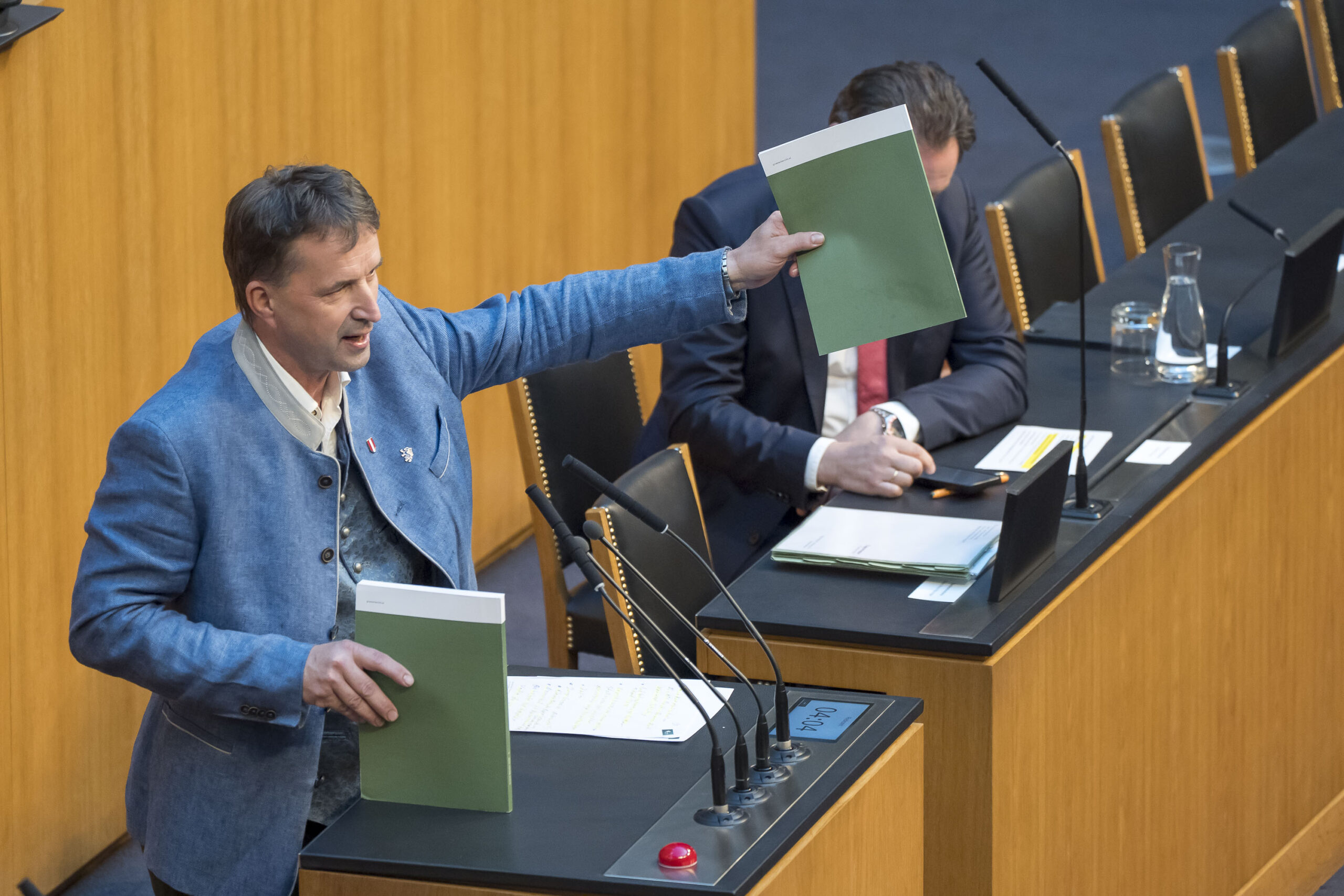 FPÖ-Abgeordneter Albert Royer hält den Grünen Bericht in der Hand, im Hintergrund Umweltminister Norbert Totschnig